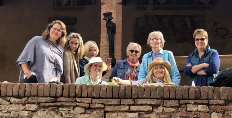 Group of women smiling outdoors near a brick wall during daytime.