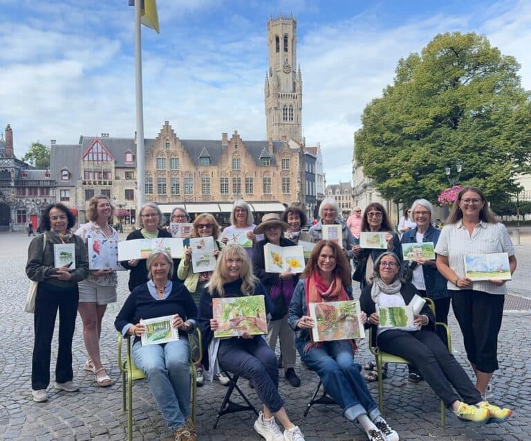 Group of women holding artwork in a historic town square with a clock tower.