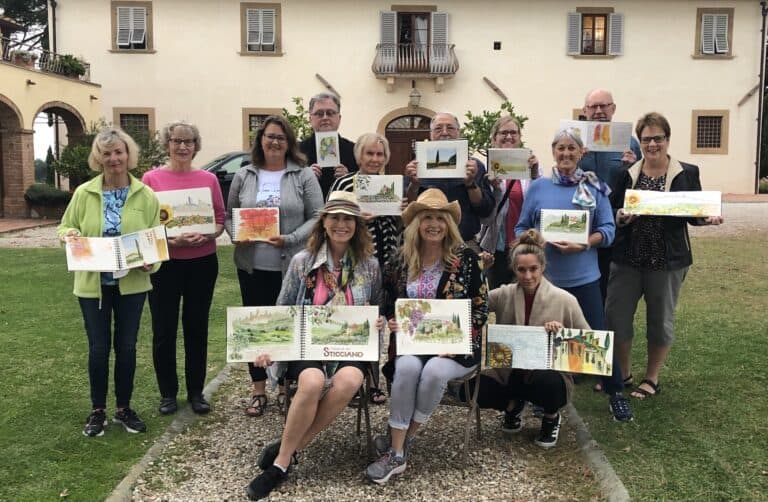 Group of people displaying their watercolor paintings outdoors in front of a building.