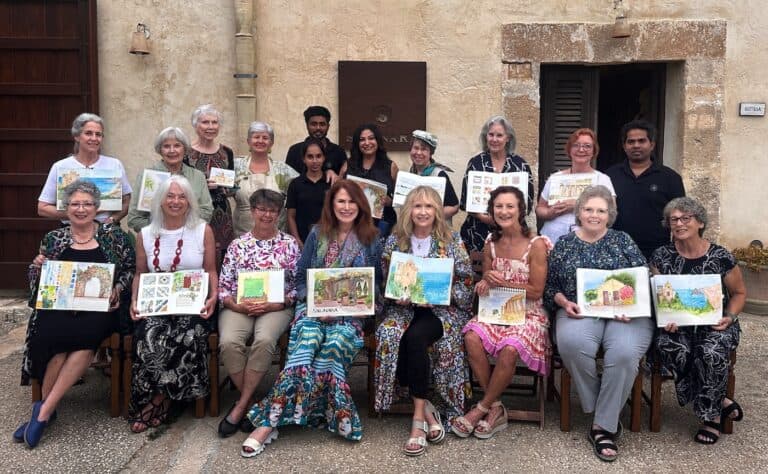 Group of women and one man holding artwork outdoors in front of a rustic wall.