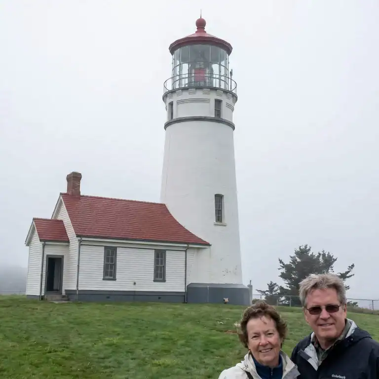 Lighthouse with two smiling visitors in front on a foggy day.