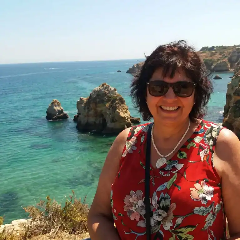 Smiling woman in sunglasses at coastal cliffs during daytime.